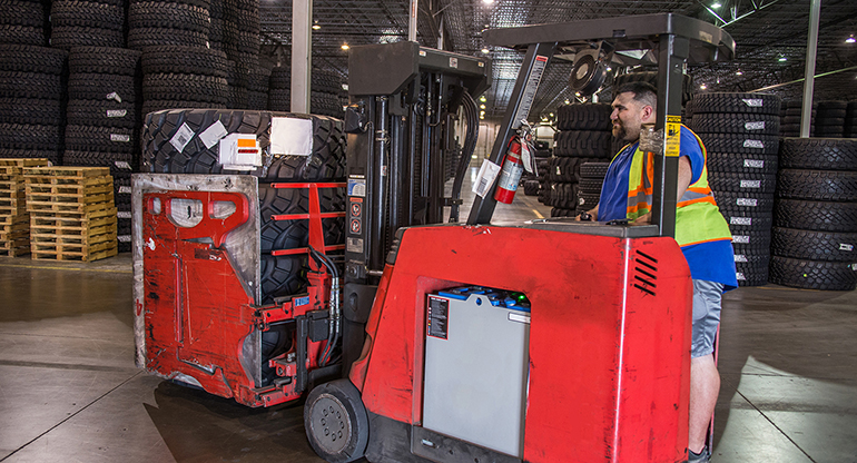 An SAIC warehouse worker prepares a set of tires for shipment onboard his forklift. 