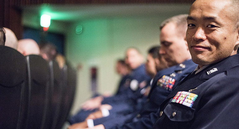 An Air Force officer sitting in a lecture looks over to the camera and smiles.