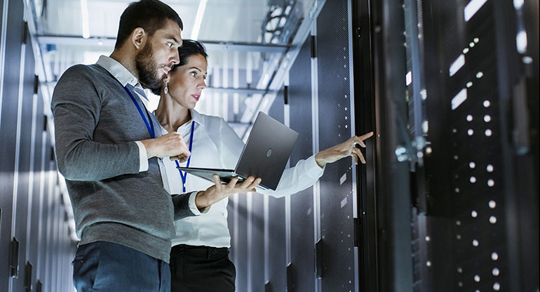 IT specialist holds laptop and discusses in the server room